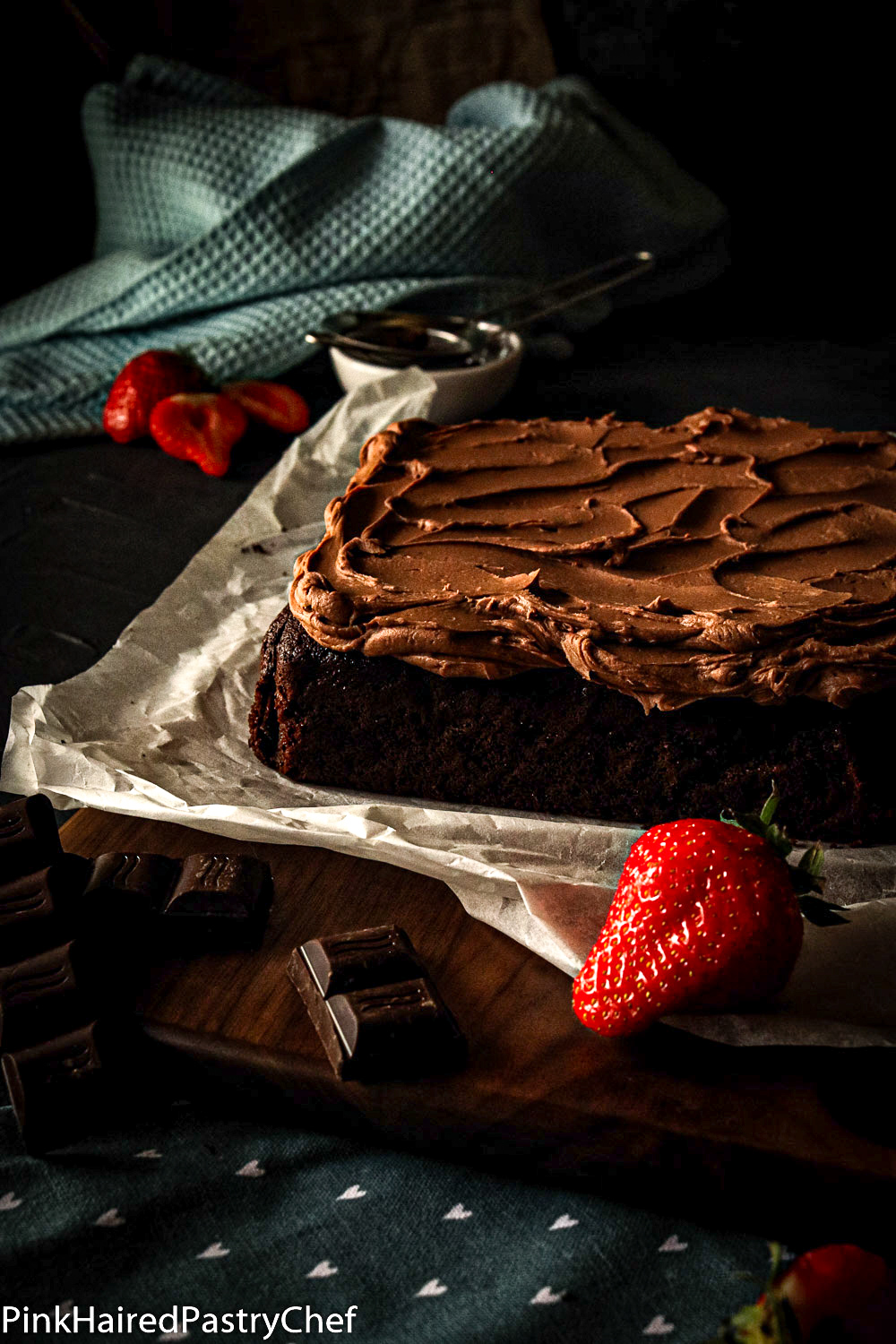 Chocolate Square Cake with Whipped Chocolate Ganache generously swirled on top. Cake resting on a piece of baking parchment. Strawberries for decoration