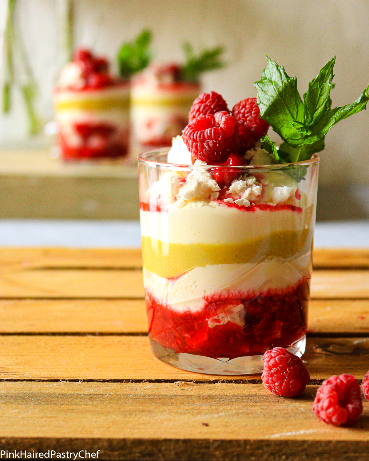 Layered Gooseberry Raspberry Eton Mess in a glass. Layers of crushed meringue, raspberry sauce, whipped cream, gooseberry curd, fresh raspberries and mint on top.